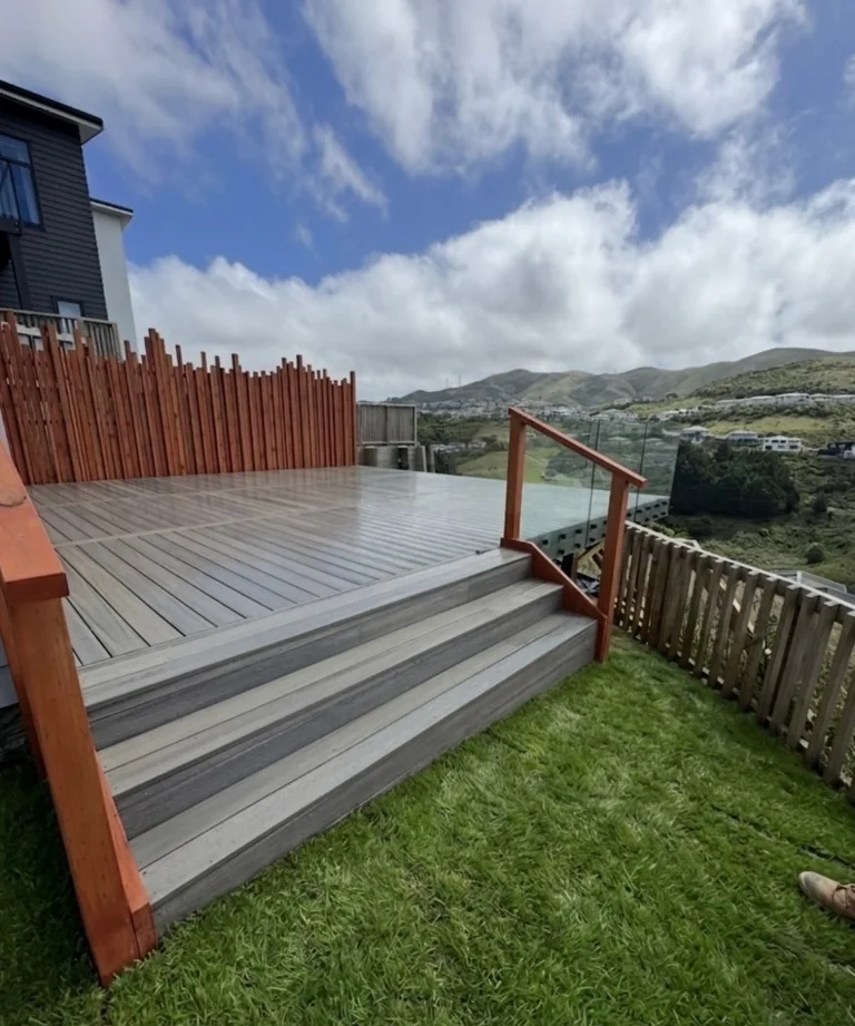 Grey deck and broad steps with a timber privacy screen, glass balustrade and hillside view